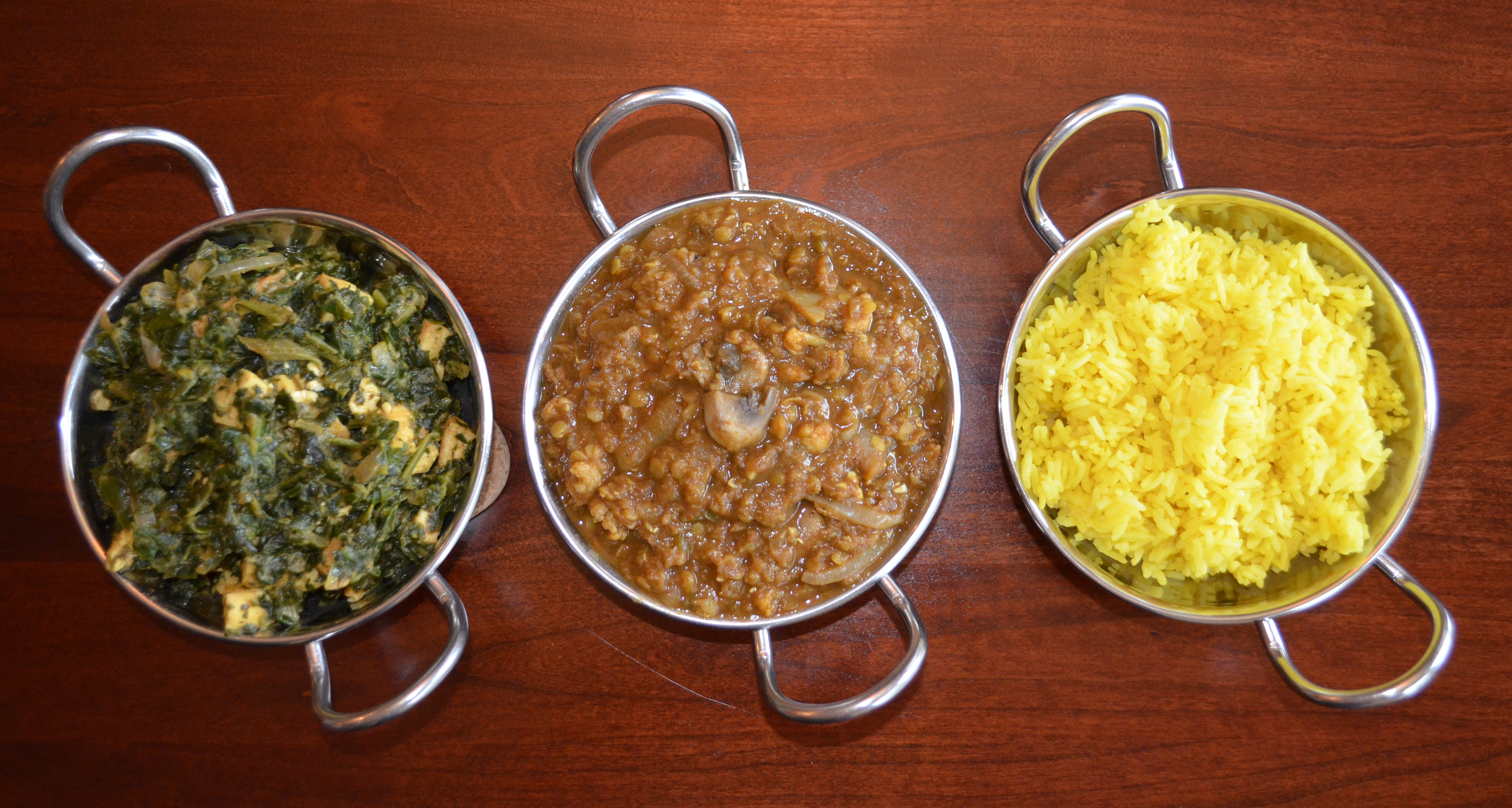 Three bowls of Indian curry and yellow rice on wooden table.